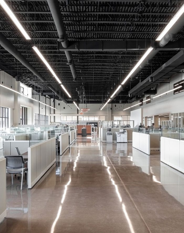 Modern open office space with high ceilings, cubicles, and polished floors, featuring ample natural lighting.