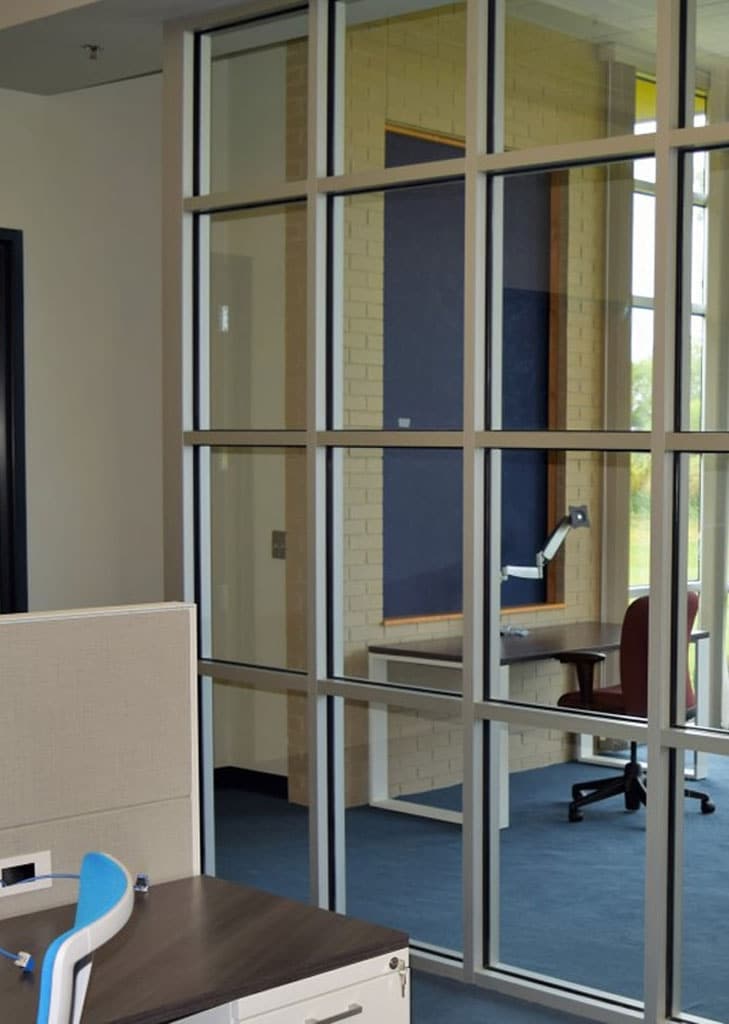 Modern office interior with glass walls, showcasing a desk and swivel chair in a shared workspace.